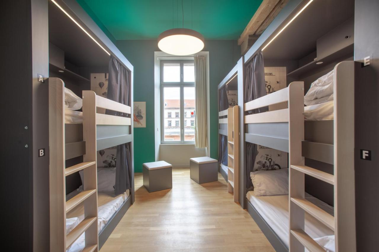 The People - Strasbourg Hostel Εξωτερικό φωτογραφία The photo shows a modern hostel room with two sets of bunk beds arranged in the style of cubicles. The beds are enclosed, providing some privacy, and each bunk features white bedding. In between the bunk beds, there are two small stools or benches. T