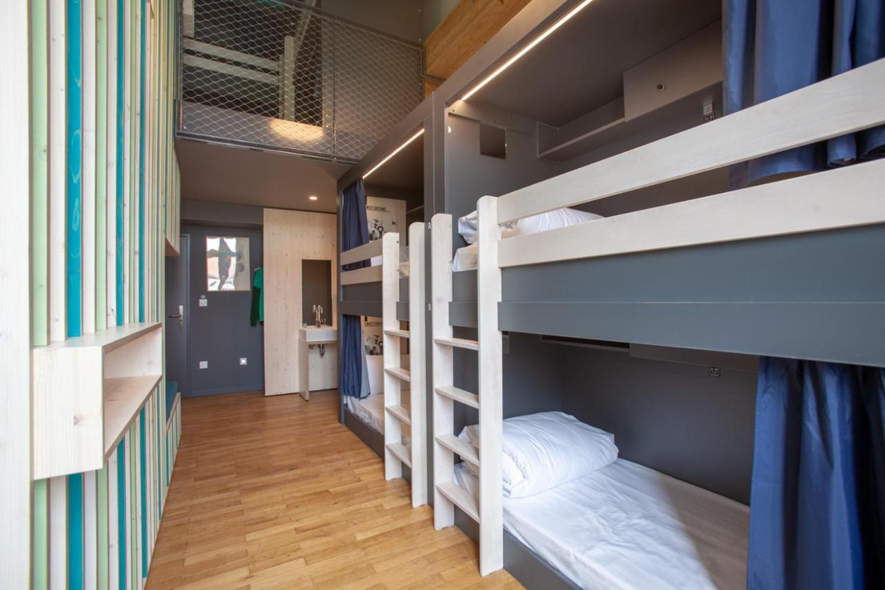 The People - Strasbourg Hostel Εξωτερικό φωτογραφία The photo shows a modern shared bedroom with two sets of bunk beds positioned along one wall. The beds have white wooden frames and neatly made bedding, with some beds featuring blue curtains for privacy. The room has wooden flooring and minimalistic