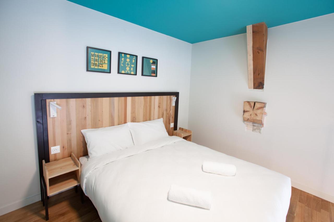 The People - Strasbourg Hostel Εξωτερικό φωτογραφία The photo shows a modern and minimalistic bedroom. The focal point is a large bed with a wooden headboard, neatly made with white bedding and two rolled towels placed on top. The walls are painted in light colors, with a bright turquoise ceiling that