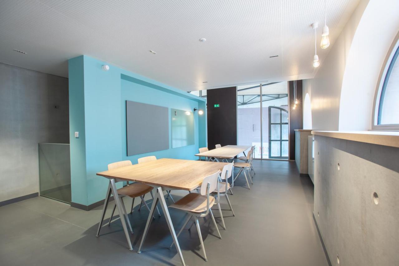 The People - Strasbourg Hostel Εξωτερικό φωτογραφία The photo shows a modern, spacious interior, which appears to be a meeting or dining area. There are several wooden tables with metal legs arranged in the space, each accompanied by white chairs. The walls are a combination of light gray and a soft t