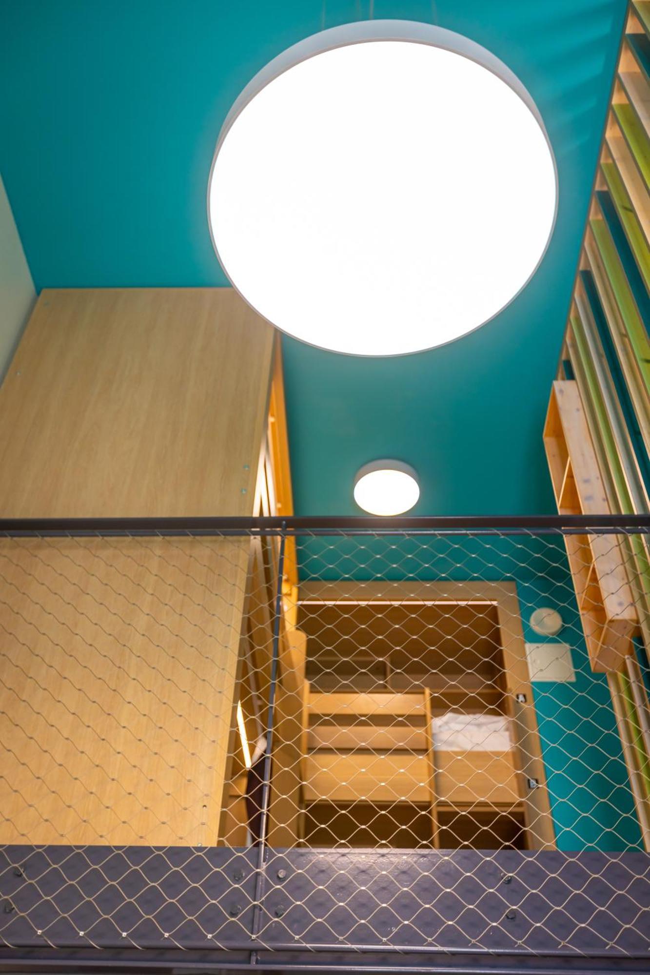 The People - Strasbourg Hostel Εξωτερικό φωτογραφία The photo shows an interior space, likely a modern home or studio. It features a bright, teal-colored wall and a large round ceiling light. To one side, there is a wooden cabinet or wardrobe, and there are shelves or storage units along the walls. A 