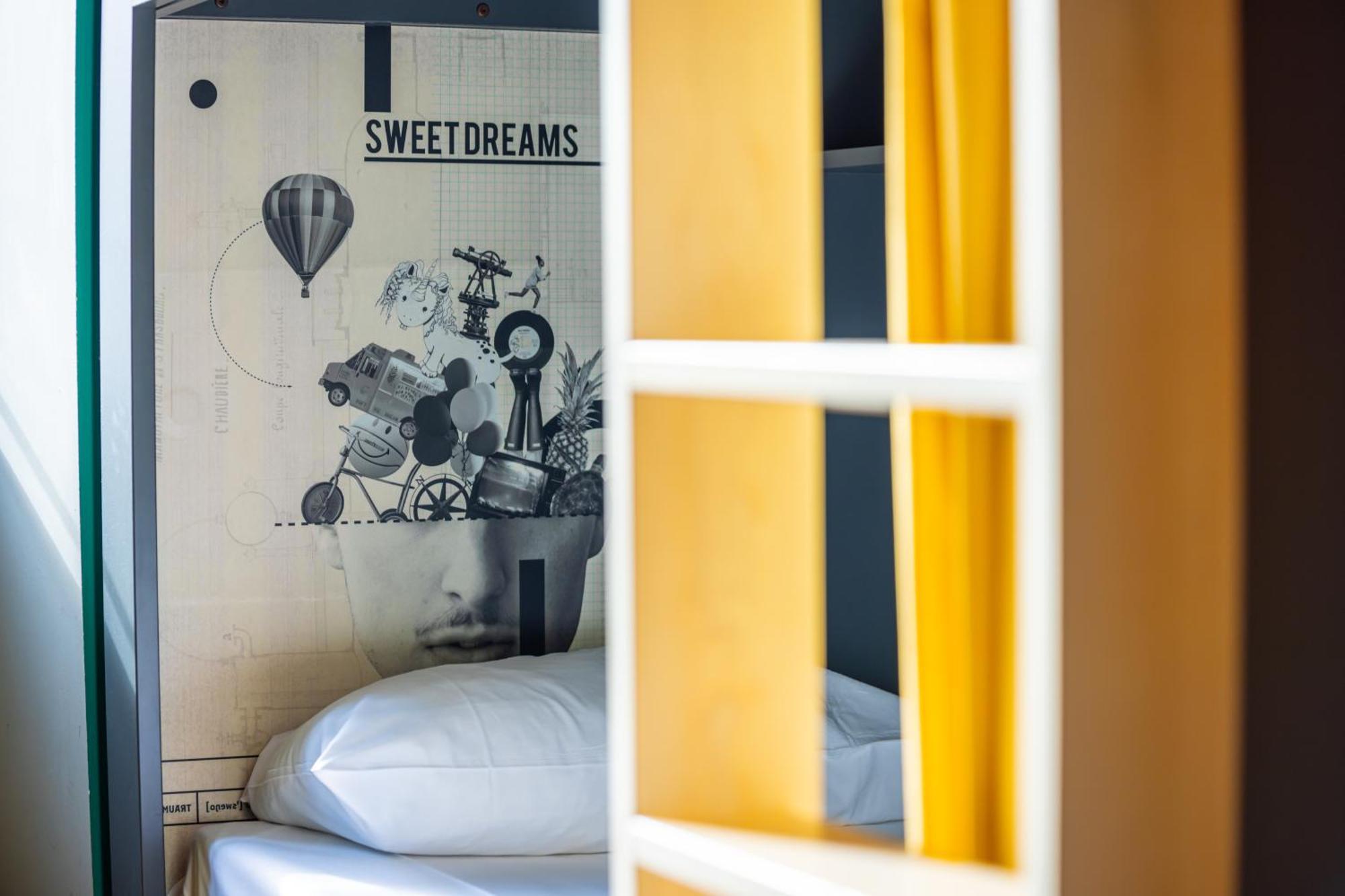 The People - Strasbourg Hostel Εξωτερικό φωτογραφία The photo shows a cozy bedroom interior with a focus on a wall decorated with artistic elements. The wall features a design that includes a collage of items like balloons and other whimsical illustrations, along with the phrase "SWEET DREAMS" at the 