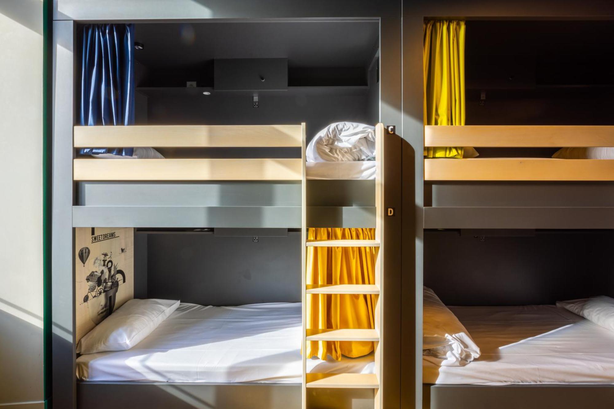 The People - Strasbourg Hostel Εξωτερικό φωτογραφία The photo shows a set of bunk beds arranged in a compact, modern layout. There are two bunk beds stacked on top of each other, with the upper and lower beds separated by a wall or partition. The top left bed has blue curtains, while the top right bed