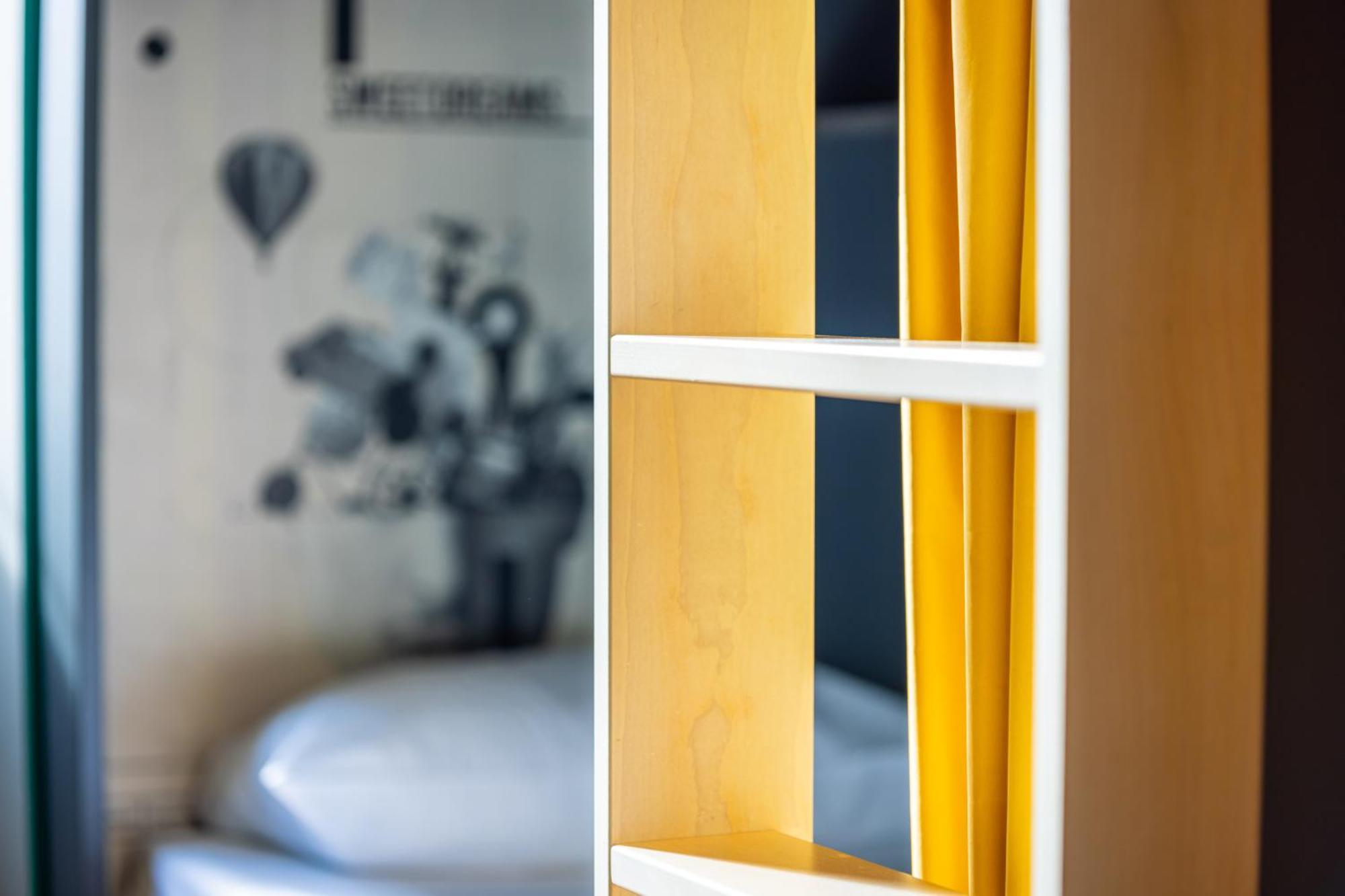 The People - Strasbourg Hostel Εξωτερικό φωτογραφία The photo shows a piece of furniture, likely a bookshelf or a storage unit, made of light-colored wood. It has several shelves, with yellow folders or files neatly placed in the compartments. In the background, there is a blurred image of a bed and s
