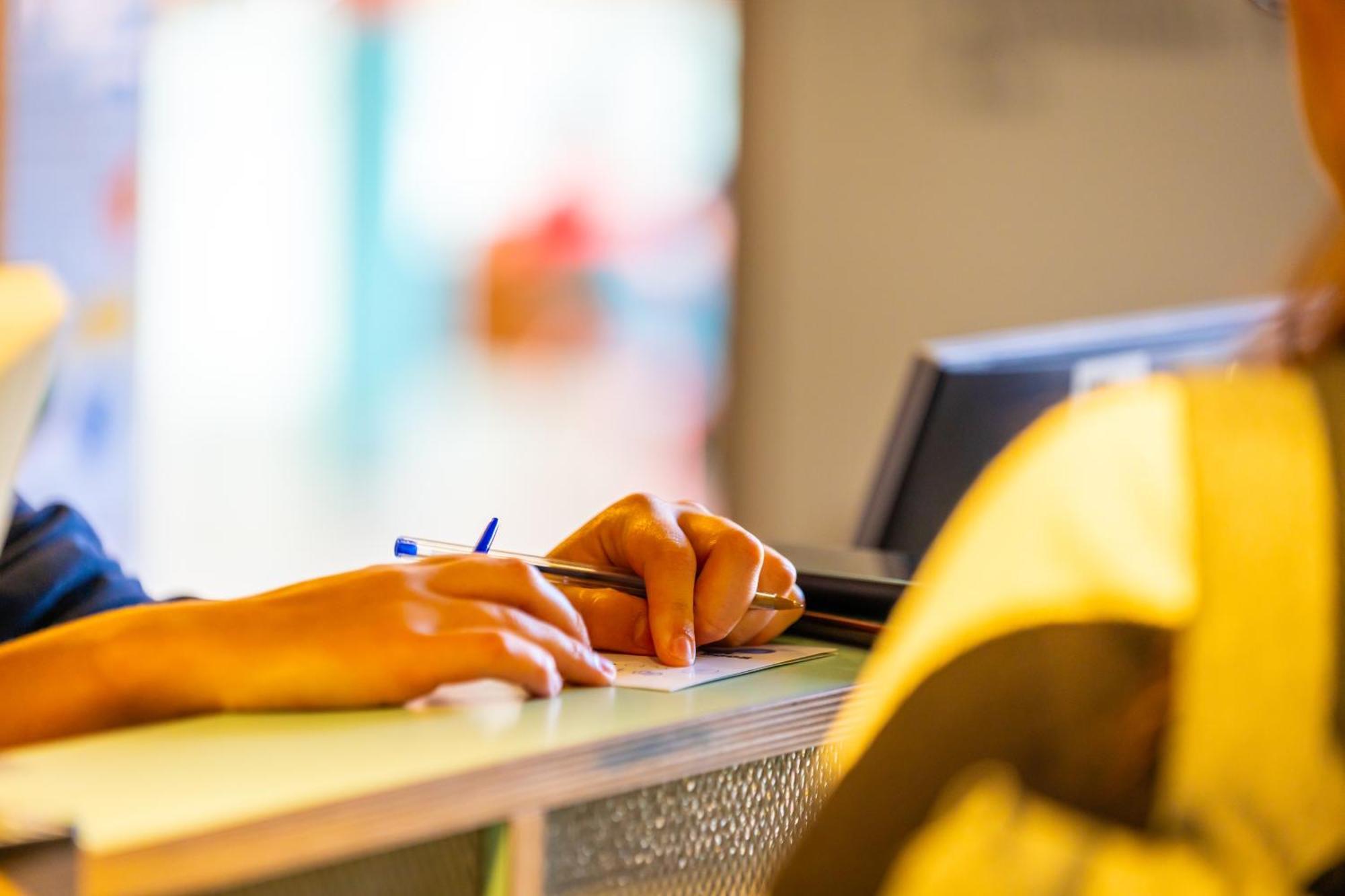 The People - Strasbourg Hostel Εξωτερικό φωτογραφία The photo shows a close-up view of a reception area. A person's hand is resting on a counter, holding a pen and a piece of paper, suggesting that they might be filling out a form or making a note. The focus is on the hand and the writing materials, w