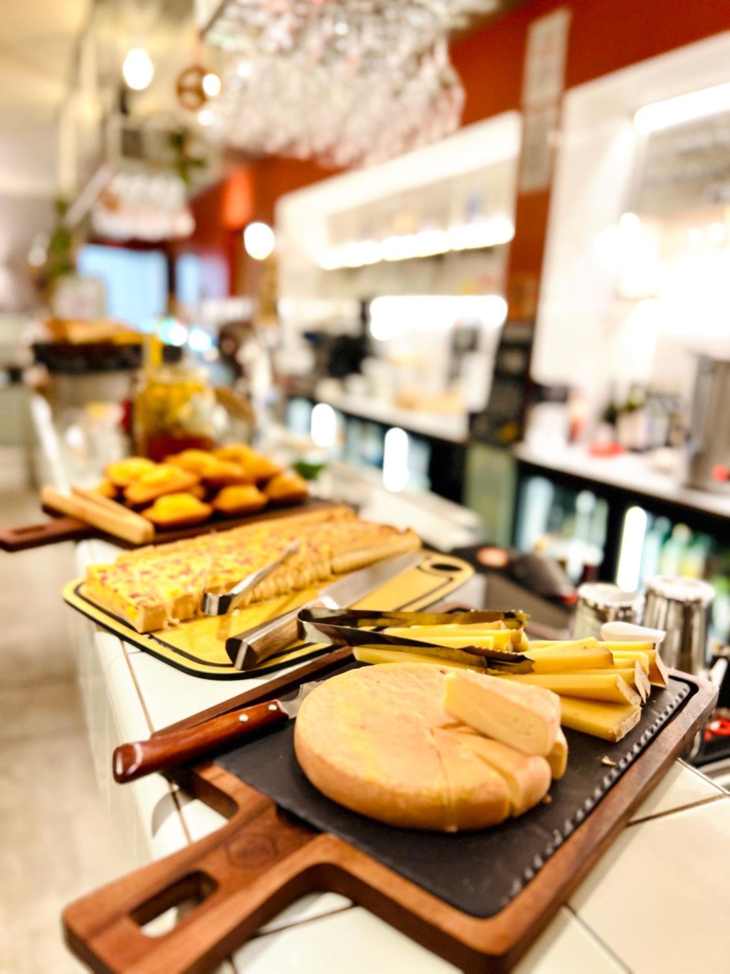 The People - Strasbourg Hostel Εξωτερικό φωτογραφία The photo shows a variety of food items arranged on a table in a stylish setting. There are several types of cheese, including round and rectangular pieces, accompanied by cheese knives. In the background, there are pastries, possibly muffins or cake